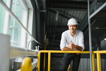 Smiling and happy employee. Industrial worker indoors in factory. Young technician with white hard hat.