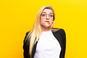 young pretty blonde woman looking puzzled and confused, biting lip with a nervous gesture, not...
