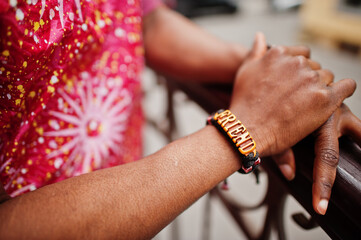 Hand with bracelet friends of a black young man wearing african traditional red colorful clothes.