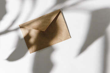 Paper envelope on white background with leaf shadow, top view