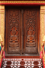 Fototapeta na wymiar Entrance door with wood carvings showing praying buddha images in a temple site in Siamese Lao PDR, Southeast Asia