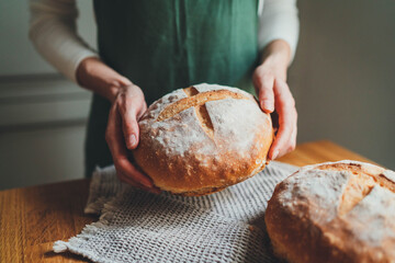 Woman holding her first homemade classic sourdough bread standing in the kitchen, Artisan Healthy...