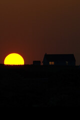 Fototapeta na wymiar large partially set yellow sun next to an isolated cottage 