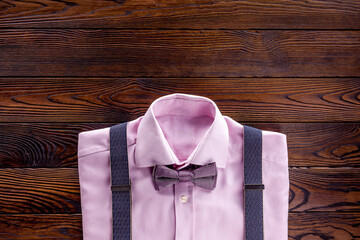 The concept of men's clothing. Pink shirt with bow-tie and suspenders on dark wooden background top view flat lay copy space