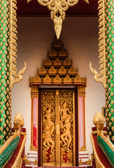 Entrance and doorway showing a golden decorated wooden ancient door with various buddha images in Siamese Lao PDR, Southeast Asia