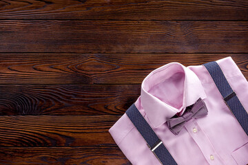 The concept of men's clothing. Pink shirt with bow-tie and suspenders on dark wooden background top view flat lay copy space