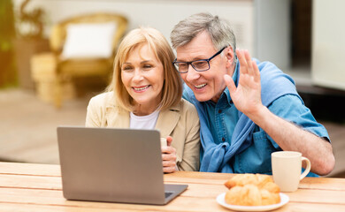 Fototapeta na wymiar Friendly mature couple chatting online via laptop near RV at campsite