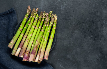 
Raw green asparagus in a black plate on a stone background with copy space for your text