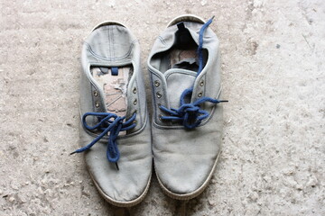 Old canvas sneakers with blue laces on a gray floor