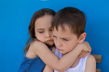 Little upset brother and sister. Isolated on a blue background. The concept of family love.