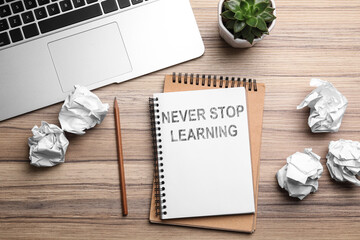 Notebook with phrase NEVER STOP LEARNING and crumpled paper on wooden table, flat lay