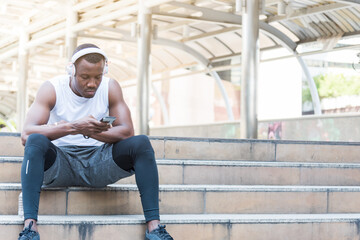 Young male athletes sitting on stairs using a smartphone And wearing headphones to listen to music.