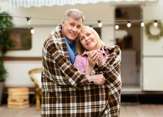 Lovely senior couple cuddling under warm blanket and hugging each other at camping site
