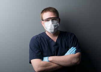 Serious lab worker in dark blue scrubs and mask with goggles and gloves takes a break 