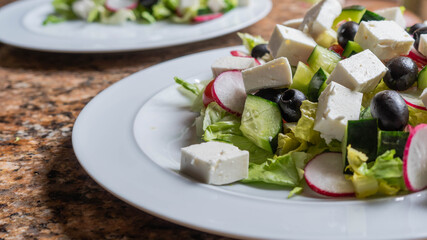 Greek salad on white plates with natural lighting on top of a granite kitchen work surface
