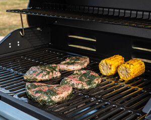Meat steak and corn on the cob grilling on a charcoal bbq