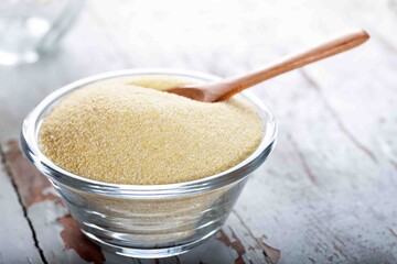 Semolina in glass bowl with spoon on wooden background.