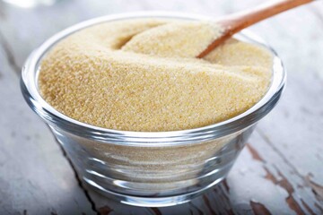 Semolina in glass bowl with spoon on wooden background.