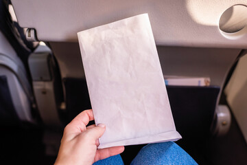 Air sickness paper bag in the hand of nauseous passenger during flight in the airplane.