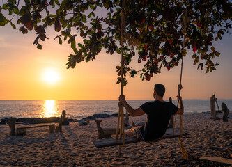 Man on a swing at sunset on the beach.
