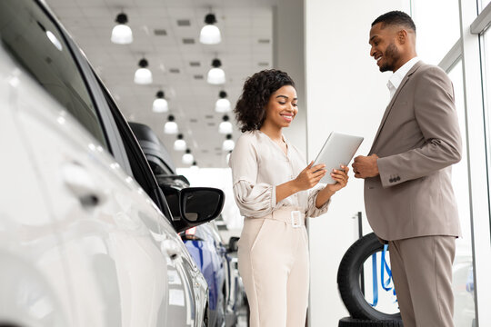 Seller Woman Showing Auto To African Businessman In Dealership Showroom