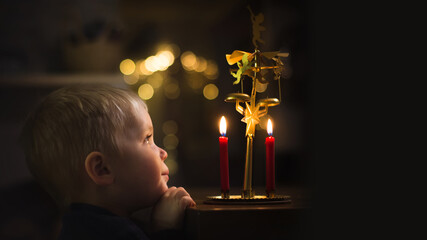 Little boy is looking at candels and angel chimes and hearing ringing, banner copy space