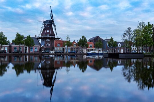 Holland - Meppel - a windmill in the middle of the town of Meppel, standing on the edge of a canal. The mill stands between the houses and is reflected in the water surface. The sky is with clouds bef