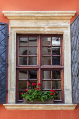 A window with dark shutters on an old building. Pots with flowers on the windowsill.