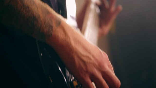 Close-up of male hands wearing tattoo playing on electric bass guitar at studio low angle