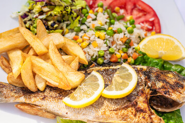 Grilled dorado fish with salad and fried potatoes on a plate