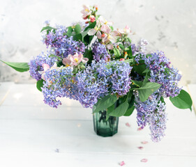Beautiful bouquet pink and lilac flowers on blurred white background with lights. Spring floral background with space for text.