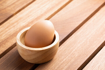 fresh raw chicken egg in a wooden bowl on a rustic brown table. concept of organic food, good health and high protein for cooking breakfast