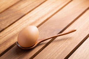 fresh raw chicken egg in a wooden spoon on a rustic brown table. concept of organic food, good health and high protein for cooking breakfast