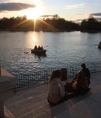 Personas navegando en bote con remos en el parque del Retiro al atardecer