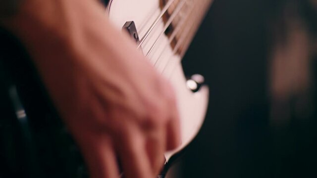 Close-up male hands of tattooed bassist guy playing on electric bass guitar at rock performance
