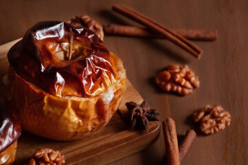 baked apples with spices, cinnamon sticks, anise, honey on a wooden tray and a brown textured background