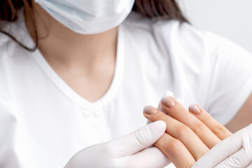 Manicurist is holding fingers of woman with beige manicure in salon.