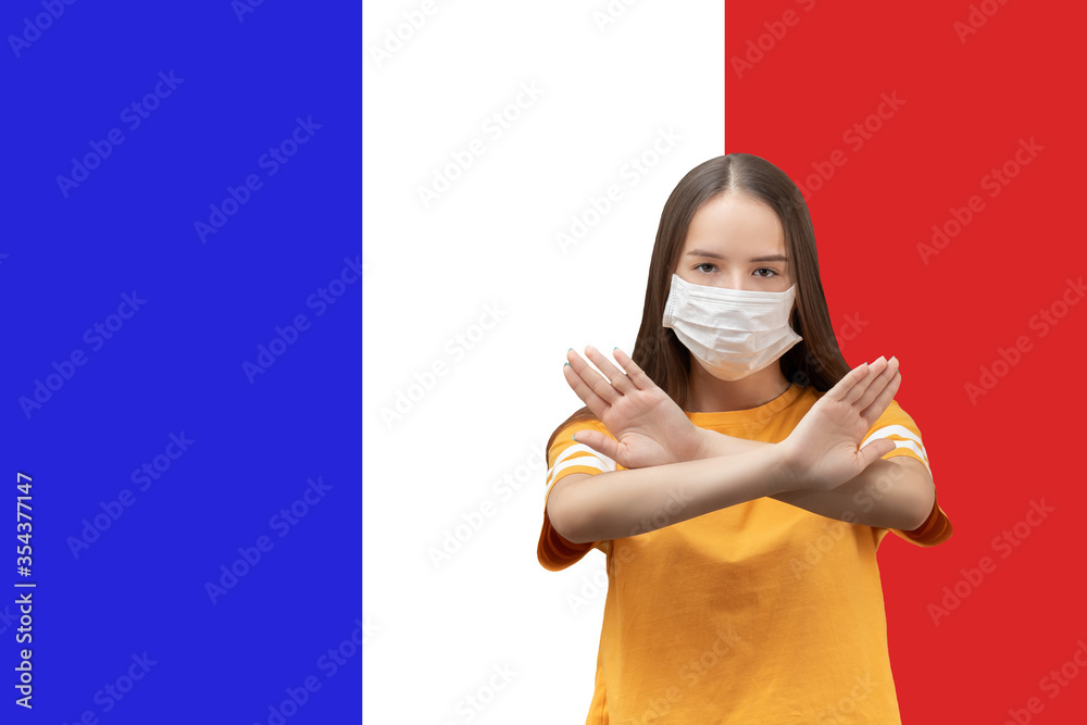 Wall mural stop the coronavirus in france. girl in antibacterial medical mask shows crossed hands on the backgr