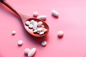 Close up of white pills on wooden spoon on pink 