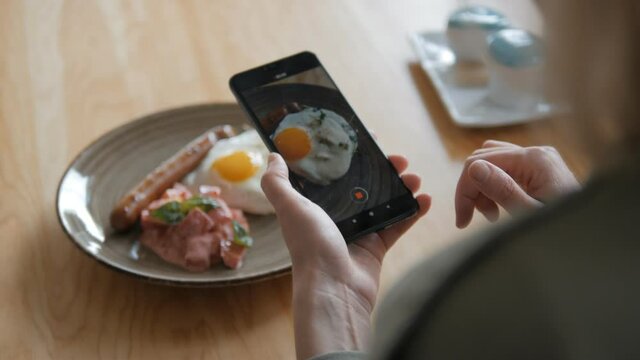 A woman using a smartphone camera takes a plate with Breakfast in a restaurant