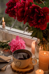 coffee, candles and peonies on a windowsill in the rain