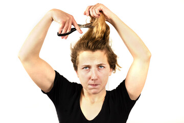 The girl is holding a pair of scissors and trying to cut her own hair. Haircut at home or on your own. isolated on a white background.