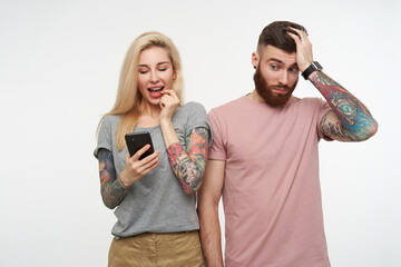 Puzzled young pretty bearded handsome man holding raised hand on his head while looking confusedly...