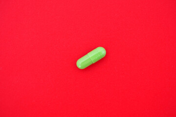 One capsule is green on an isolated red background. Concept of medical treatment.