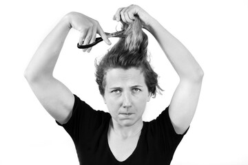The girl is holding a pair of scissors and trying to cut her own hair. Haircut at home or on your own. isolated on a white background