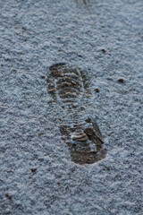 Human single footprint in white fresh winter snow. top view. Simple trace of boot in fallen snow. shoeprint on icy ground left by walking man. one imprint on snowy road. Fresh snow fallen on asphalt