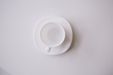 A white cup for tea or coffee on the white plate on the white table or background. flat lay. still life