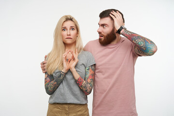 Bewildered young pretty blonde tattooed lady biting worringly underlip while looking confusedly at...