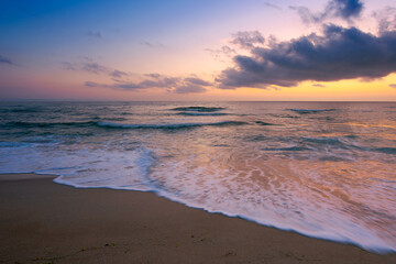 sea scenery at sunset. beautiful landscape of sandy beach in purple dusk. wave running on to the shore. clouds on the  sky above horizon.