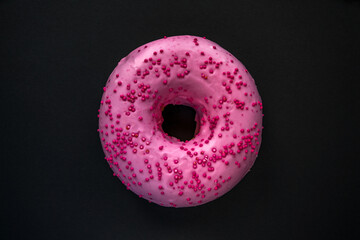 pink donut with topping on a black background. Sweets, high sugar content. Minimalist picture.